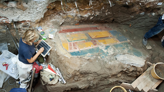Archaeologist Luciana Jacobelli studies a large collapsed fresco fragment. The visible side of the painting probably decorated the wall of an as-yet unidentified room, while the opposite side, now embedded in the ground, was featured in the triclinium.